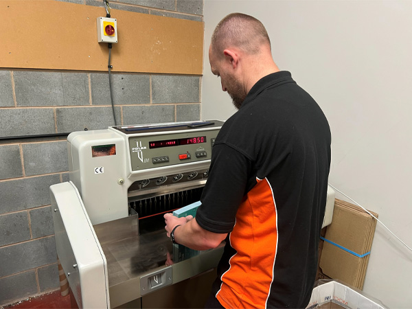 Team member Gary using a polar industrial guillotine for printed funeral orders of service.